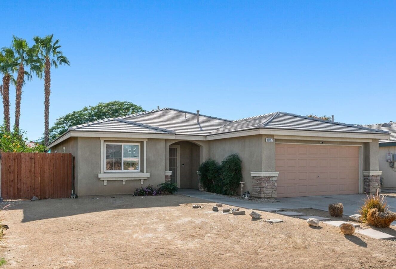A single-story house with a garage, a front yard with landscaping, and a clear sky.