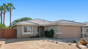 A single-story house with a garage, a front yard with landscaping, and a clear sky.