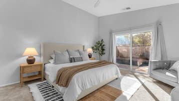 A bedroom with a bed, bedside lamps, a large window, and a view of the outdoors.