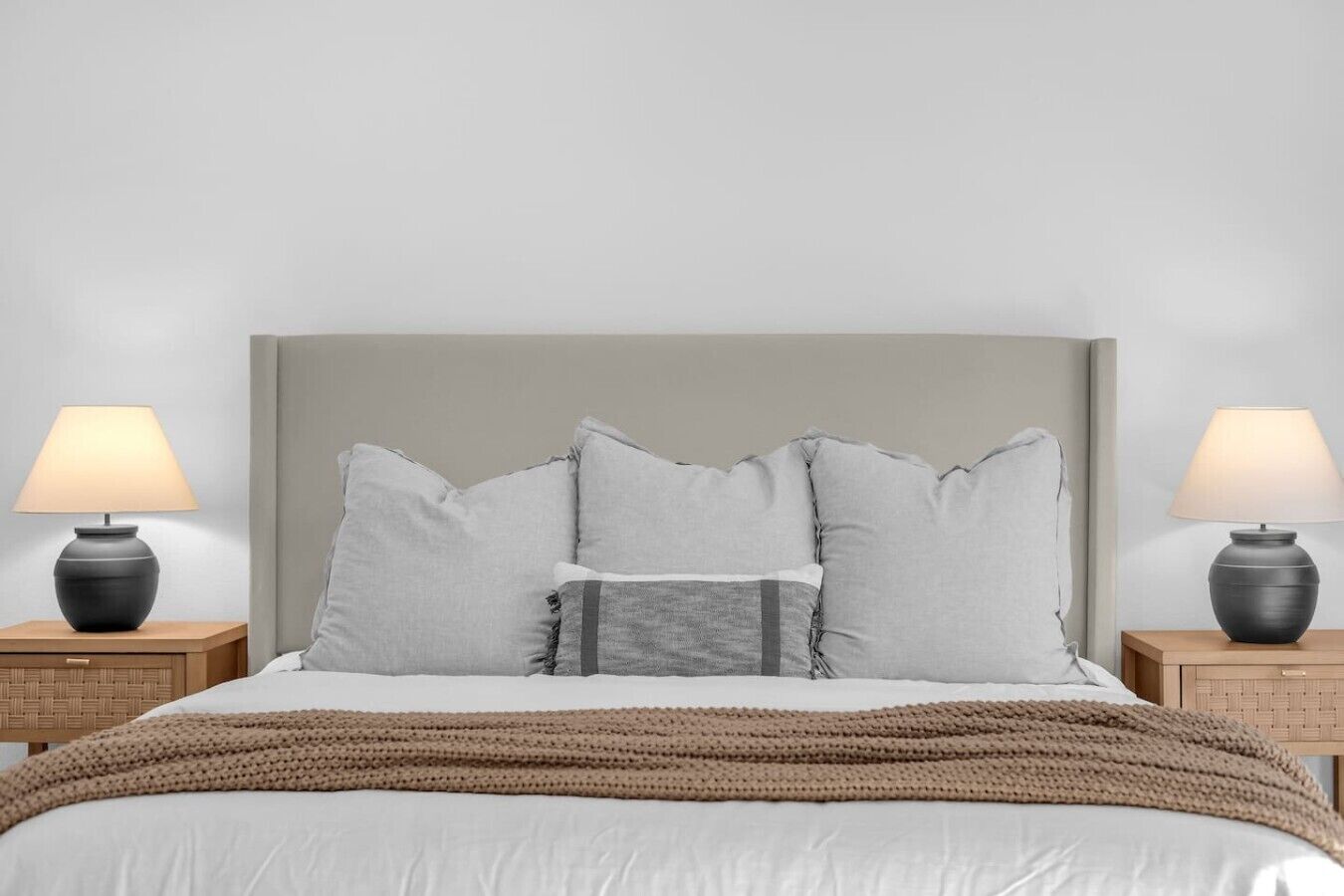 A bed with a grey headboard, two bedside tables with lamps, and a brown knitted throw.