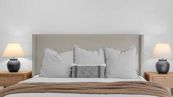 A bed with a grey headboard, two bedside tables with lamps, and a brown knitted throw.