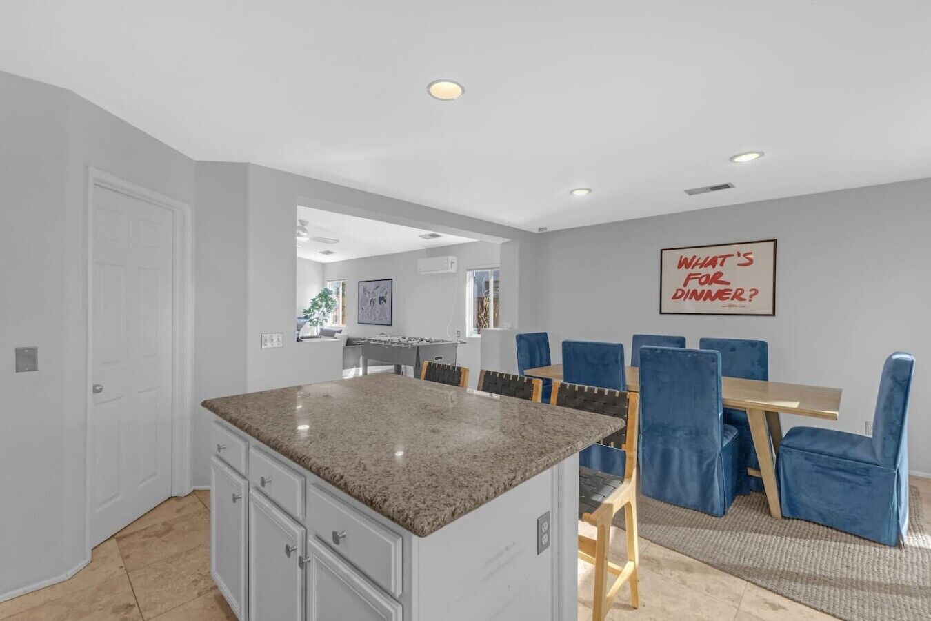 A modern kitchen with granite countertops, a dining area with blue chairs, and a wall-mounted sign.