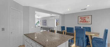 A modern kitchen with granite countertops, a dining area with blue chairs, and a wall-mounted sign.