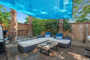 A patio with a large blue shade sail, wicker furniture, and a wooden table. - Early Check-In. AC Comfort + Pool, Spa +FAST WIFI (Coachella)