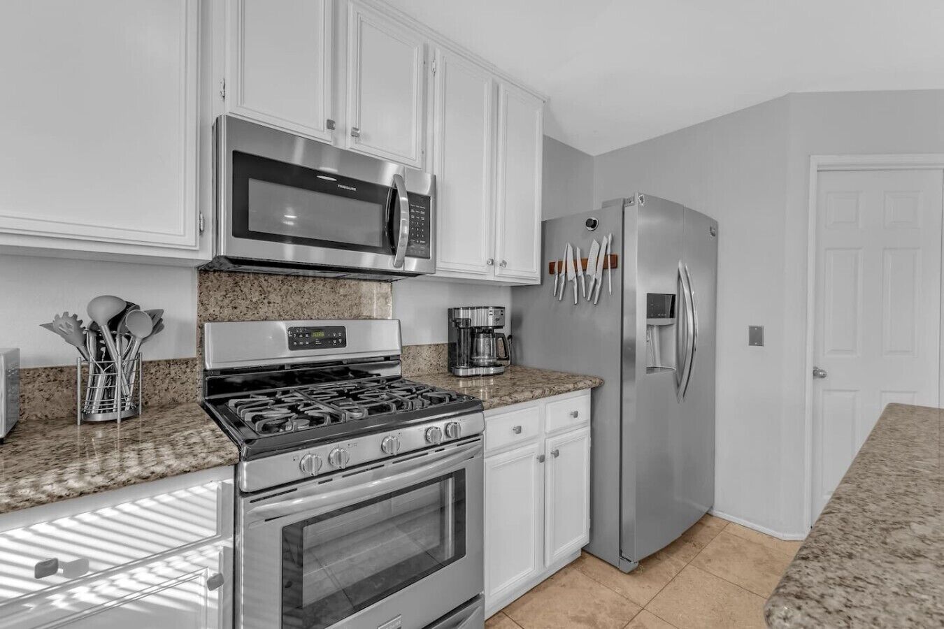 A kitchen with white cabinets, a stainless steel stove, a microwave, a refrigerator, and a coffee maker.
