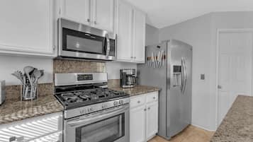 A kitchen with white cabinets, a stainless steel stove, a microwave, a refrigerator, and a coffee maker.