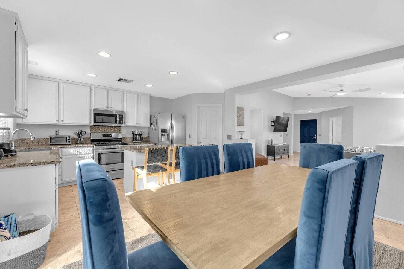 A modern kitchen with white cabinets, a microwave, and a stove. There is a dining area with a wooden table and blue upholstered chairs.