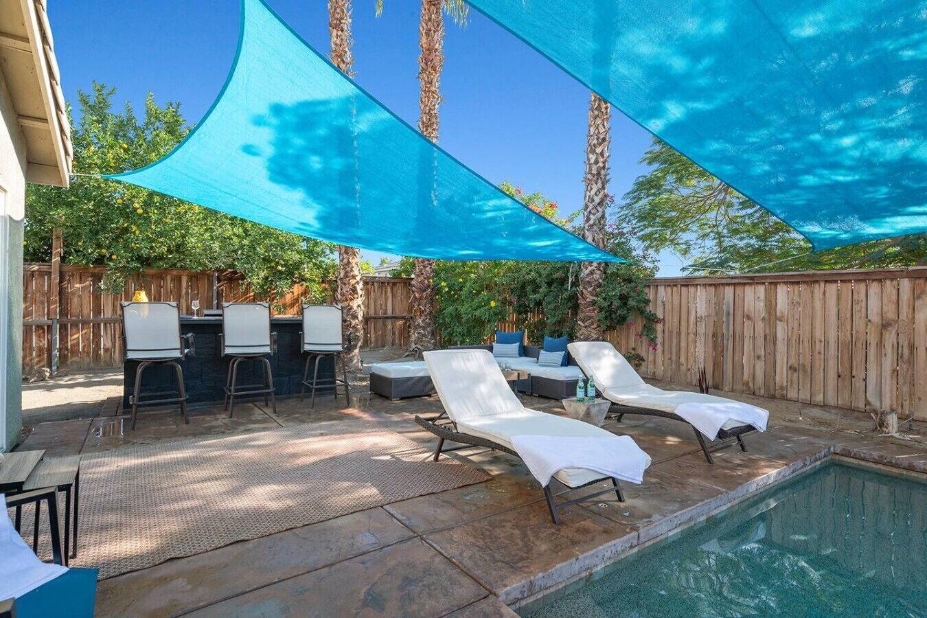 An outdoor pool area with lounge chairs, a barbecue setup, and a shaded canopy.