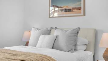 Ein Bett mit weißer Decke und Kissen, einer beige farbenen Tagesdecke und einem gerahmten Bild von einer Diner-Kneipe an der Wand.