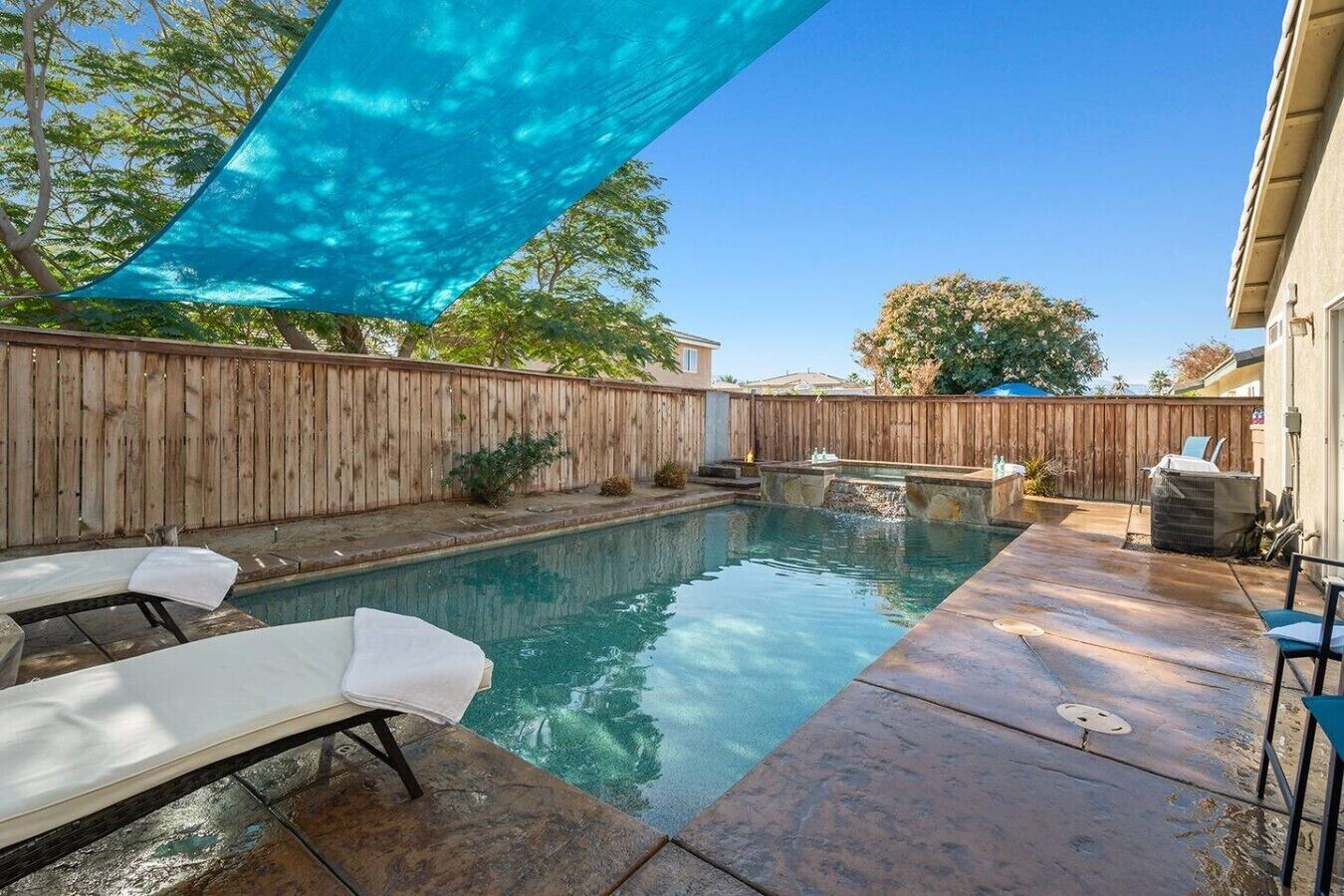 A backyard with a swimming pool, a wooden fence, and a covered patio area.