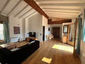 Een ruime woonkamer met houten vloeren, een zwarte bank, een televisie en een houten kast.