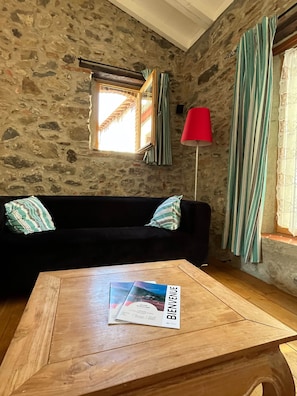 Ein Zimmer mit einer Steinsturz, einem schwarzen Sofa mit gestreiften Kissen, einem hölzernen Couchtisch mit einer Zeitschrift, einer roten Stehlampe und einem Fenster mit Vorhängen.