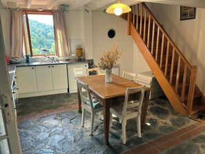 Een keuken met witte kasten, een houten eettafel en een trap.