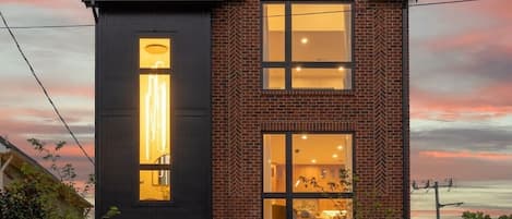 Un edificio de dos plantas con fachada de ladrillo y ventanas grandes, presenta un diseño moderno con techo plano y una chimenea visible.