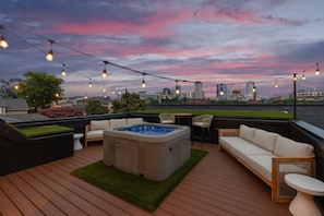 A rooftop deck with a hot tub, seating area, and string lights against a city skyline at dusk. - 6 Bedroom Home with a City Skyline View, Hot Tub + Pool Table (Nashville)