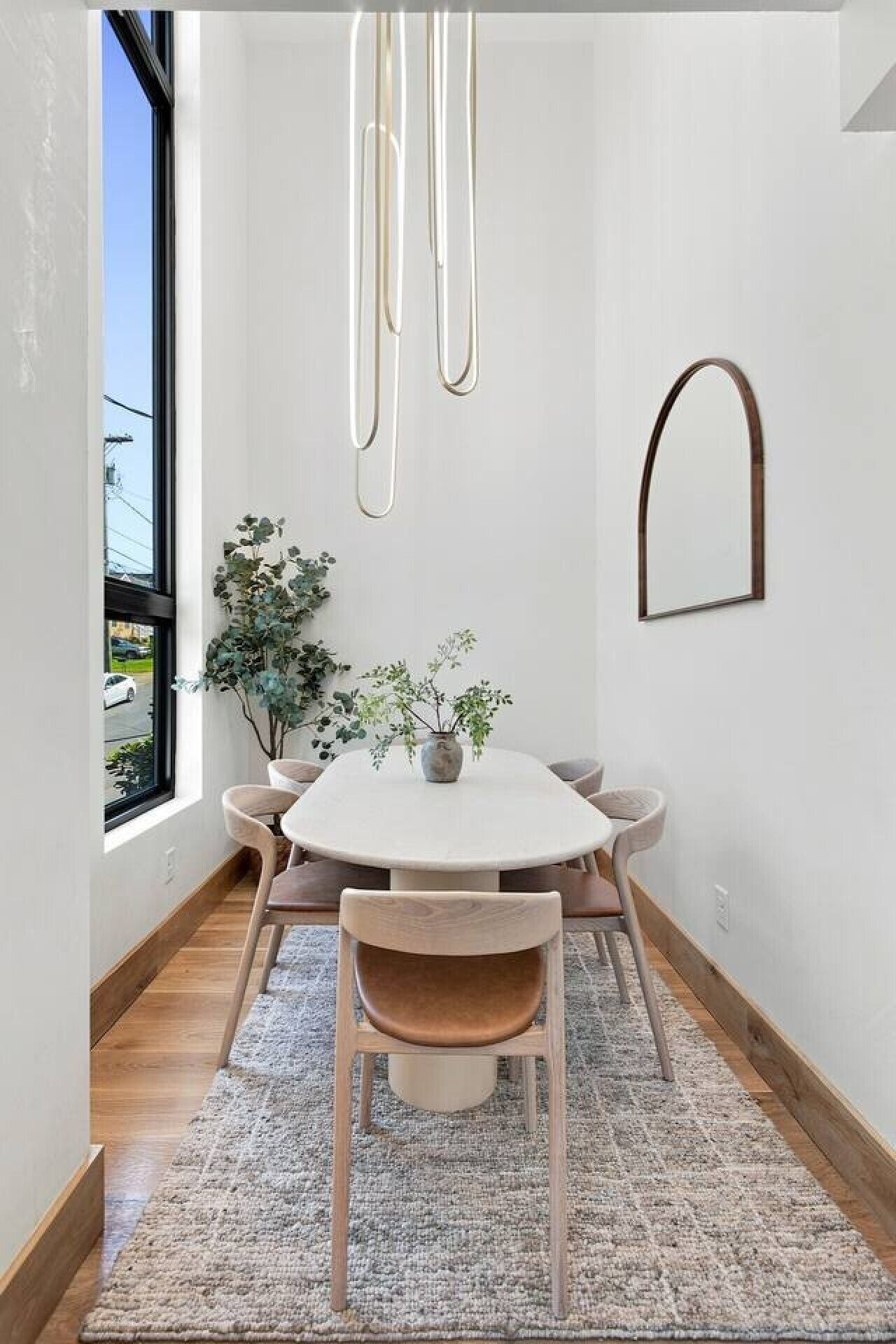 Un coin repas avec une table ronde, des chaises, un vase avec des plantes, un luminaire suspendu et une vue par la fenêtre.