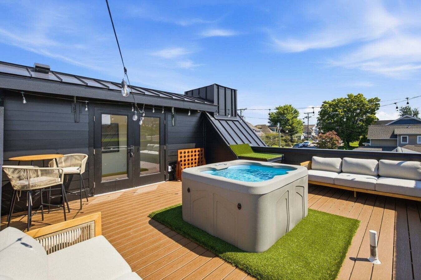A rooftop deck with a hot tub, outdoor seating, and a view of the neighborhood.