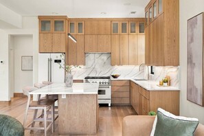 A modern kitchen with wooden cabinets, a marble countertop, and a central island with bar stools. - 6 Bedroom Home with a City Skyline View, Hot Tub + Pool Table (Nashville)