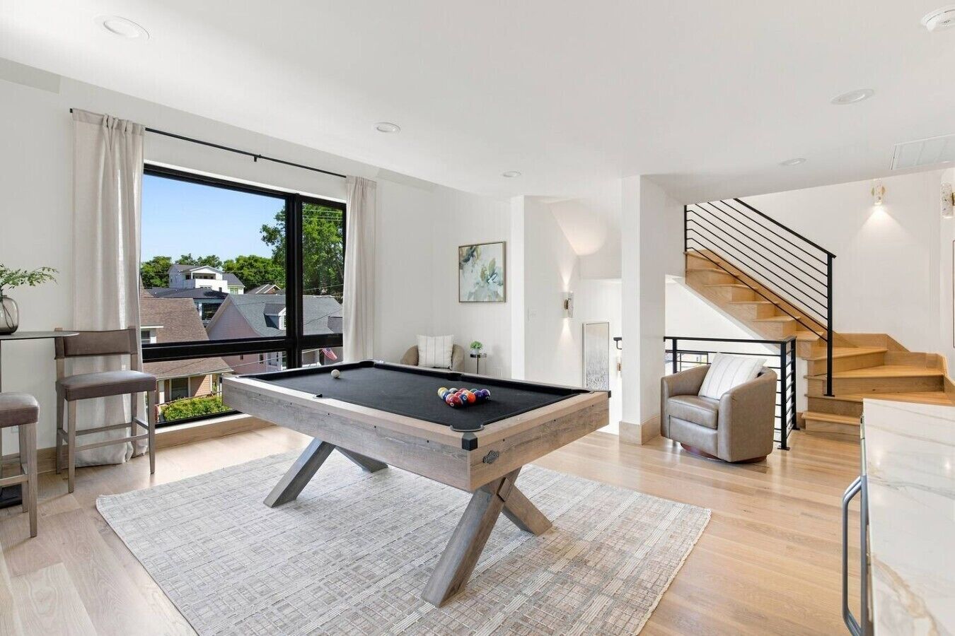 A modern living room with a pool table, a staircase, and a view of the outside.