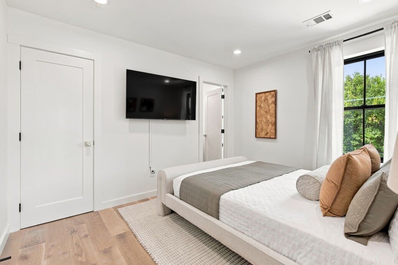 A bedroom with a bed, a television mounted on the wall, a window with curtains, and a door.
