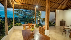An outdoor patio with a wooden table and chairs, surrounded by plants and a view of the landscape. - Kayun Retreat Mas Suite (Ubud)