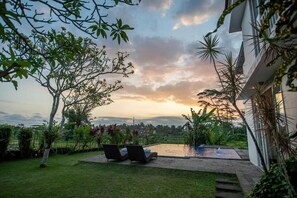 A pool area with lounge chairs, surrounded by lush greenery and a view of distant hills.