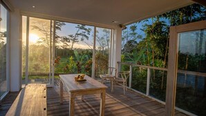 A spacious balcony with a wooden table and chairs, large windows offering a view of the surrounding greenery. - Kayun Retreat Mas Suite (Mas)