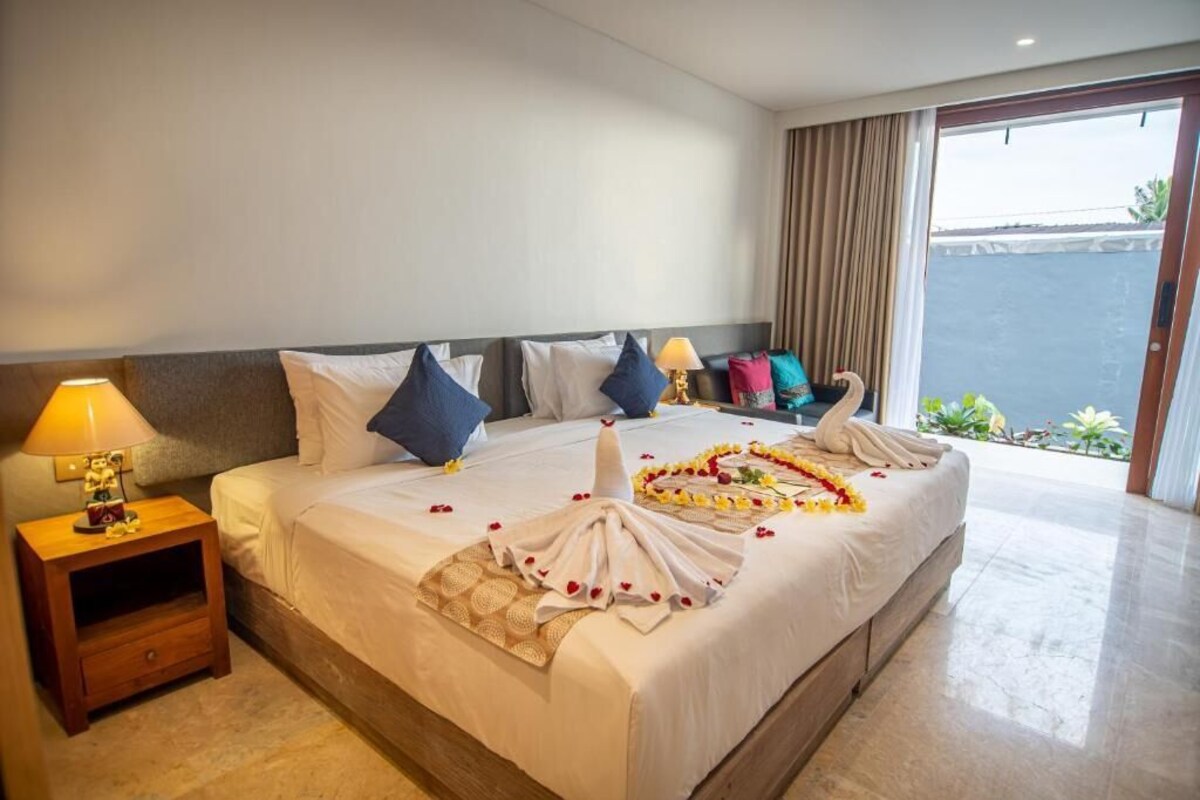 Een hotelkamer met een groot bed, een nachtkastje met een lamp en uitzicht op zee door een schuifdeur.