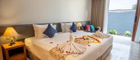 Habitación de hotel con una cama grande, una mesita de noche con lámpara y vistas al mar a través de una puerta corrediza.