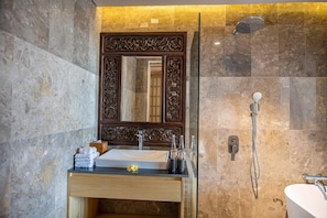 Een badkamer met een marmeren wand, een houten wastafelmeubel, een grote spiegel, een douche en een toilet.