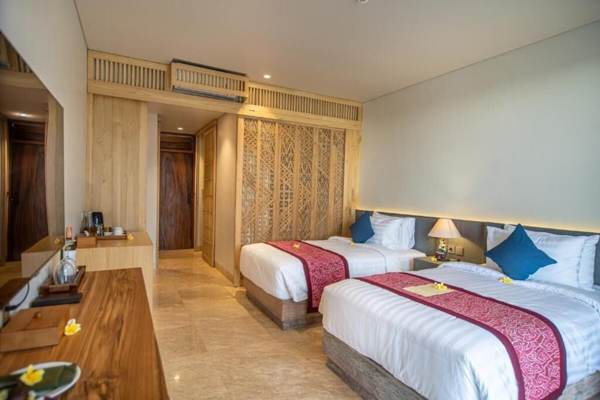 Een hotelkamer met twee bedden, een houten bureau en een decoratieve roomdivider.