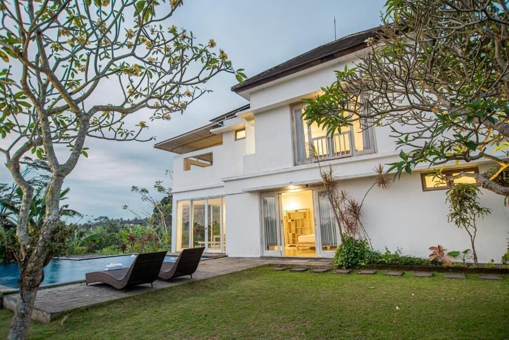 Une maison moderne à deux étages dotée d’une piscine, d’un espace salon extérieur et d’une végétation luxuriante.
