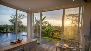 A room with a large sliding glass door leading to a pool and garden, a wooden table, and a round table with chairs. - Kayun Retreat Mas Suite (Mas)