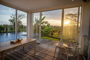 A room with a large sliding glass door leading to a pool and garden, a wooden table, and a round table with chairs. - Kayun Retreat Mas Suite (Mas)
