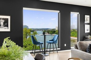 A modern living room with a large window, two blue chairs, a round table, and a sofa. - Stunning Riverview Condo - Walk to Downtown, Garage, Private Balcony (Nashville)