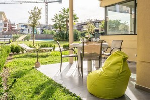 Eine Terrasse im Freien mit Tisch und Stühlen, einem grünen Sitzsack und Blick auf eine Baustelle im Hintergrund.