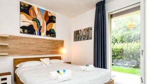 A hotel room with a bed, artwork on the wall, and a view of greenery through a glass door. - Oasi del Garda in Desenzano - Pool, Garden, and Garage (Desenzano del Garda)