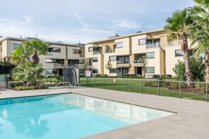 A modern apartment building with a swimming pool, palm trees, and a clear sky. - Oasi del Garda in Desenzano - Pool, Garden, and Garage (Desenzano del Garda)