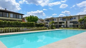 A swimming pool with a tiled deck, surrounded by apartment buildings and greenery. - Oasi del Garda in Desenzano - Pool, Garden, and Garage (Desenzano del Garda)