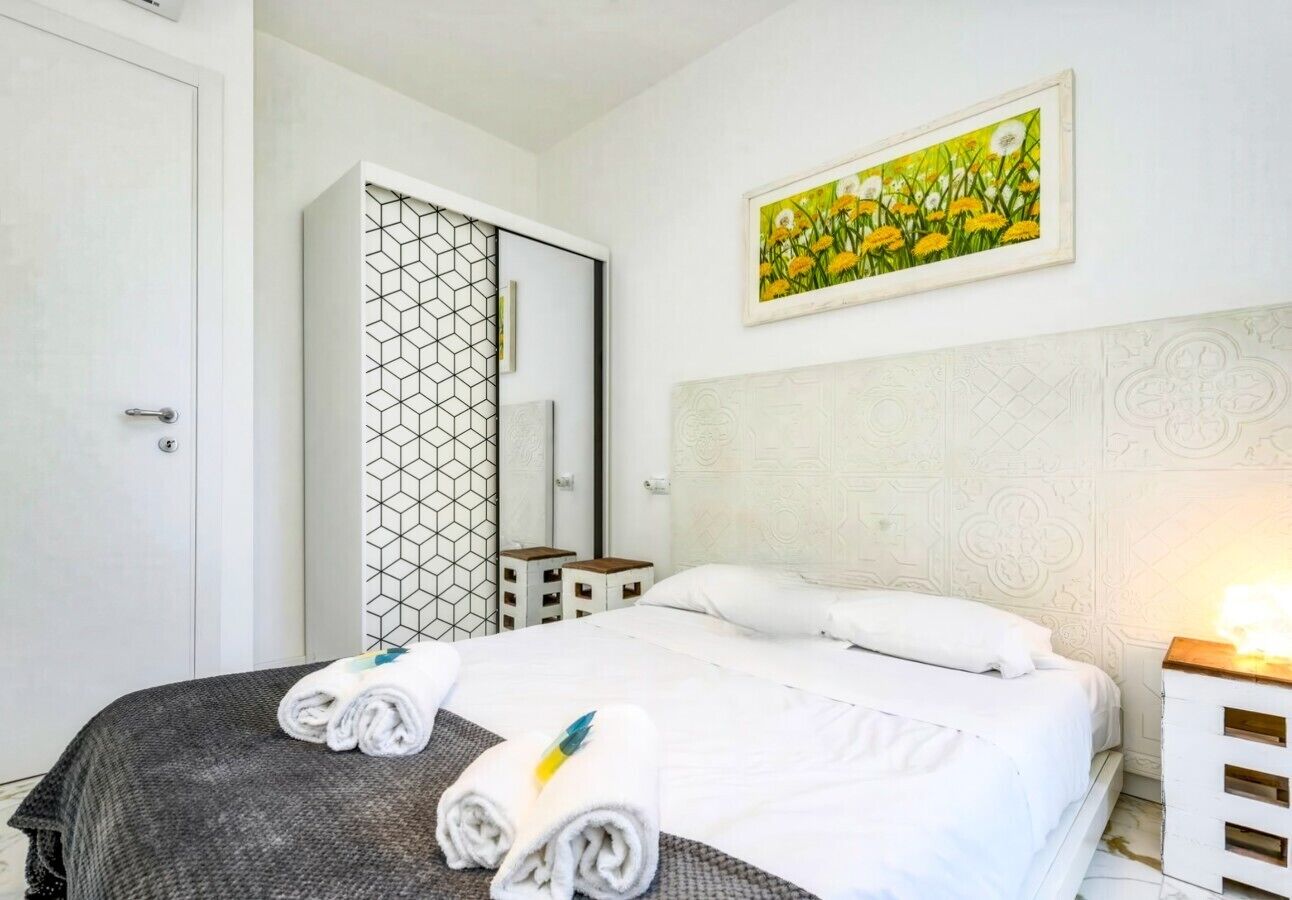 A hotel room with a bed, a wardrobe, a bedside table, and a painting on the wall.