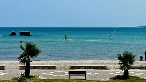 A beach with clear blue water, palm trees, and a paved walkway with benches. - At Antico Molo Sea View: A cozy apartment near the beach. (San Cataldo)