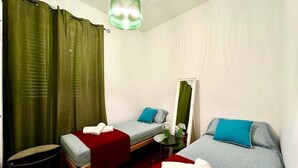 A hotel room with two single beds, a small table, a chair, a mirror, and a green curtain. - At Antico Molo Sea View: A cozy apartment near the beach. (San Cataldo)