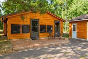 En timmerstuga med en veranda, två dörrar och en liten sittplats utomhus.