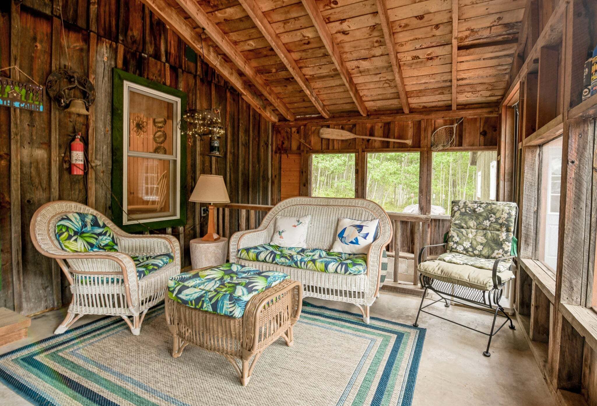 A rustic cabin interior with wicker furniture, a fire extinguisher, and a view of the forest.