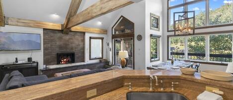A spacious living area with a fireplace, a large window, and a kitchen with a sink and counter.