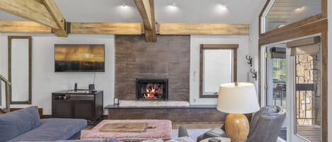 Una sala de estar con chimenea, un sofá, una mesa con lámpara y vistas a través de un ventanal.