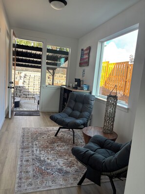 Een moderne woonkamer met een groot raam, een zwarte leren fauteuil, een kamerbreed tapijt en een houten salontafel.