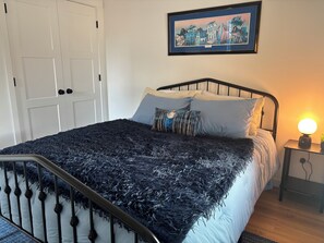 Ein Schlafzimmer mit einem Bett, einem Nachttisch, einem gerahmten Bild an der Wand und einer Tür.
