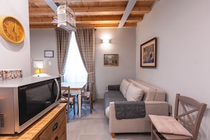 Un espacio habitable compacto con techo de madera, un área de comedor con mesa y sillas, un sofá, un microondas, un reloj y un cuadro en la pared.
