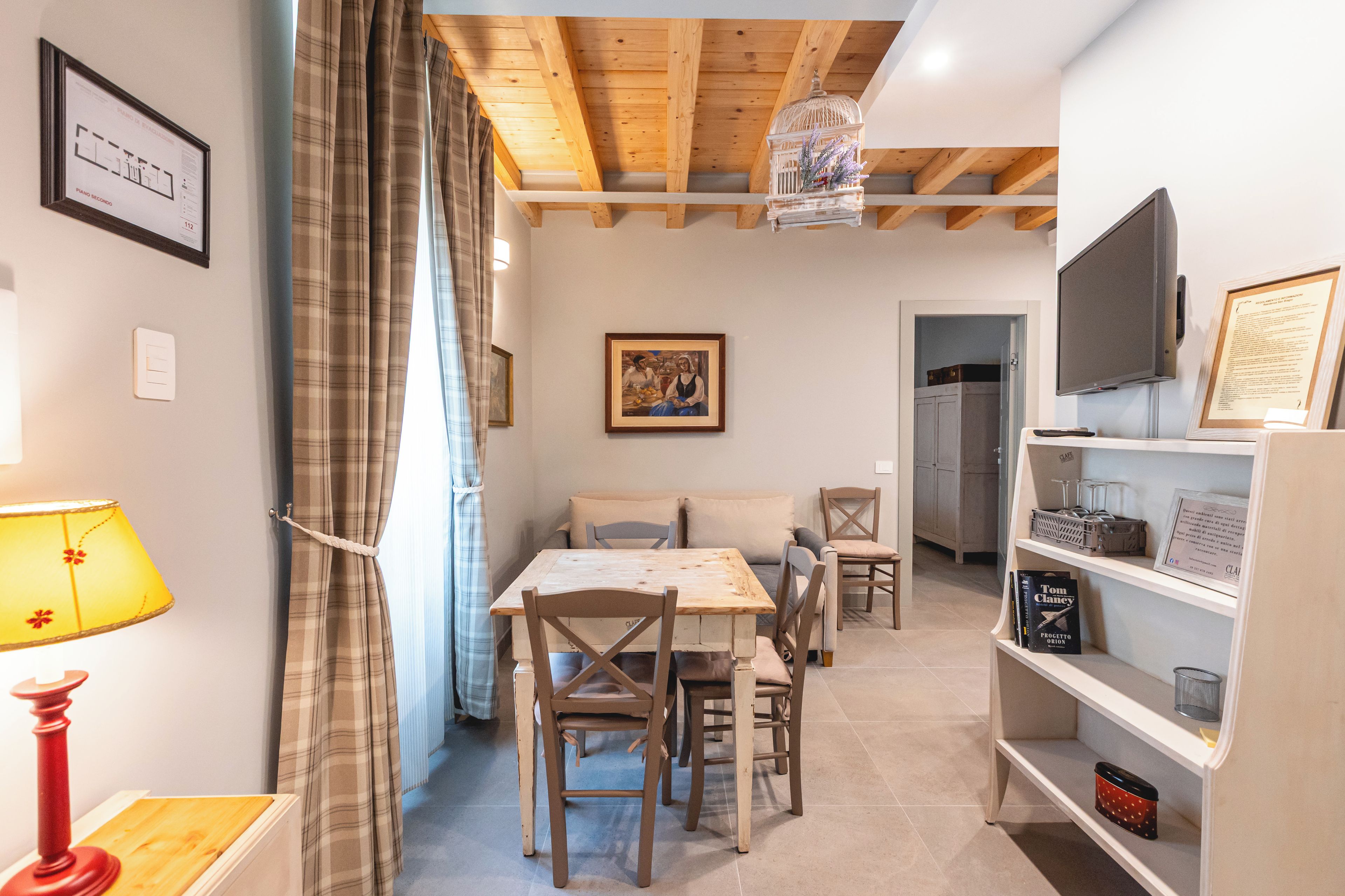 Una camera accogliente con soffitto in legno, un tavolo da pranzo con sedie, una televisione e una libreria.